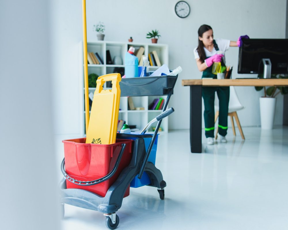 young-female-janitor-cleaning-office-with-various-cleaning-equipment.jpg